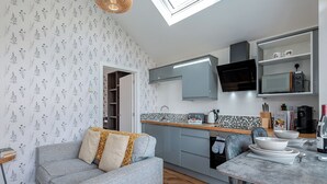 A compact kitchen with grey cabinets, a dining table, and a sofa with patterned cushions.