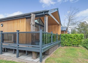 A wooden building with a balcony, a brick wall, and a hedge in the yard.