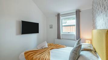 Une chambre à coucher avec un lit, une télévision, une fenêtre avec des rideaux et un radiateur.