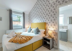 A bedroom with a bed, bedside table, lamp, and a view of the outside.