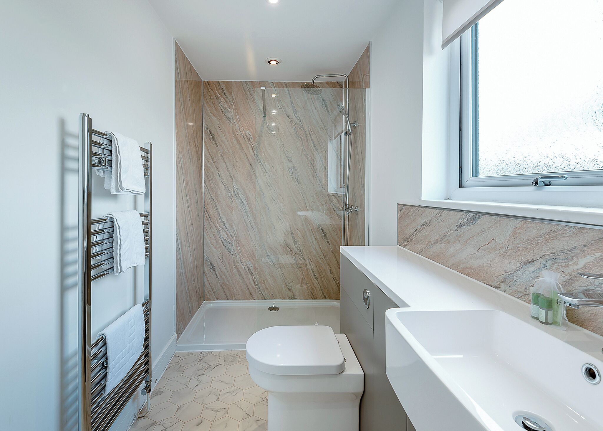 Une salle de bain moderne équipée d’une douche, de toilettes et d’un lavabo, avec des murs en marbre et une grande fenêtre.