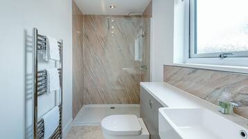 Une salle de bain moderne équipée d’une douche, de toilettes et d’un lavabo, avec des murs en marbre et une grande fenêtre.