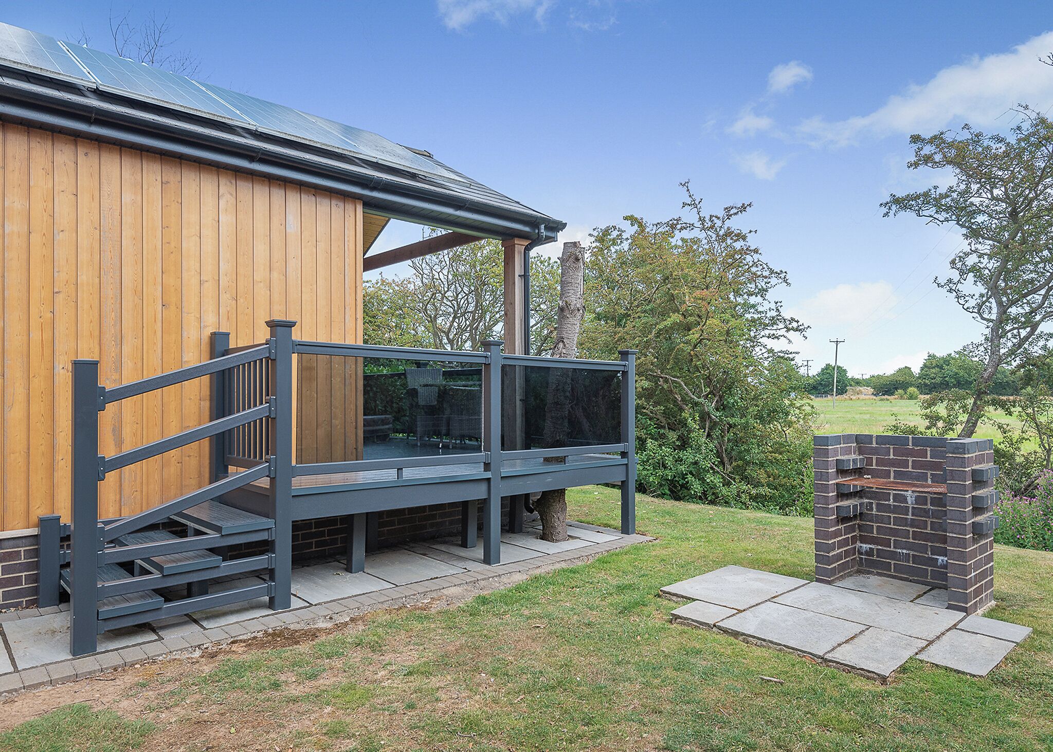 A wooden building with a balcony, a brick barbecue area, and a clear sky.