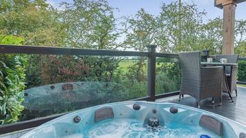 Un bain à remous sur une terrasse, avec vue sur la verdure, et une table avec des chaises.