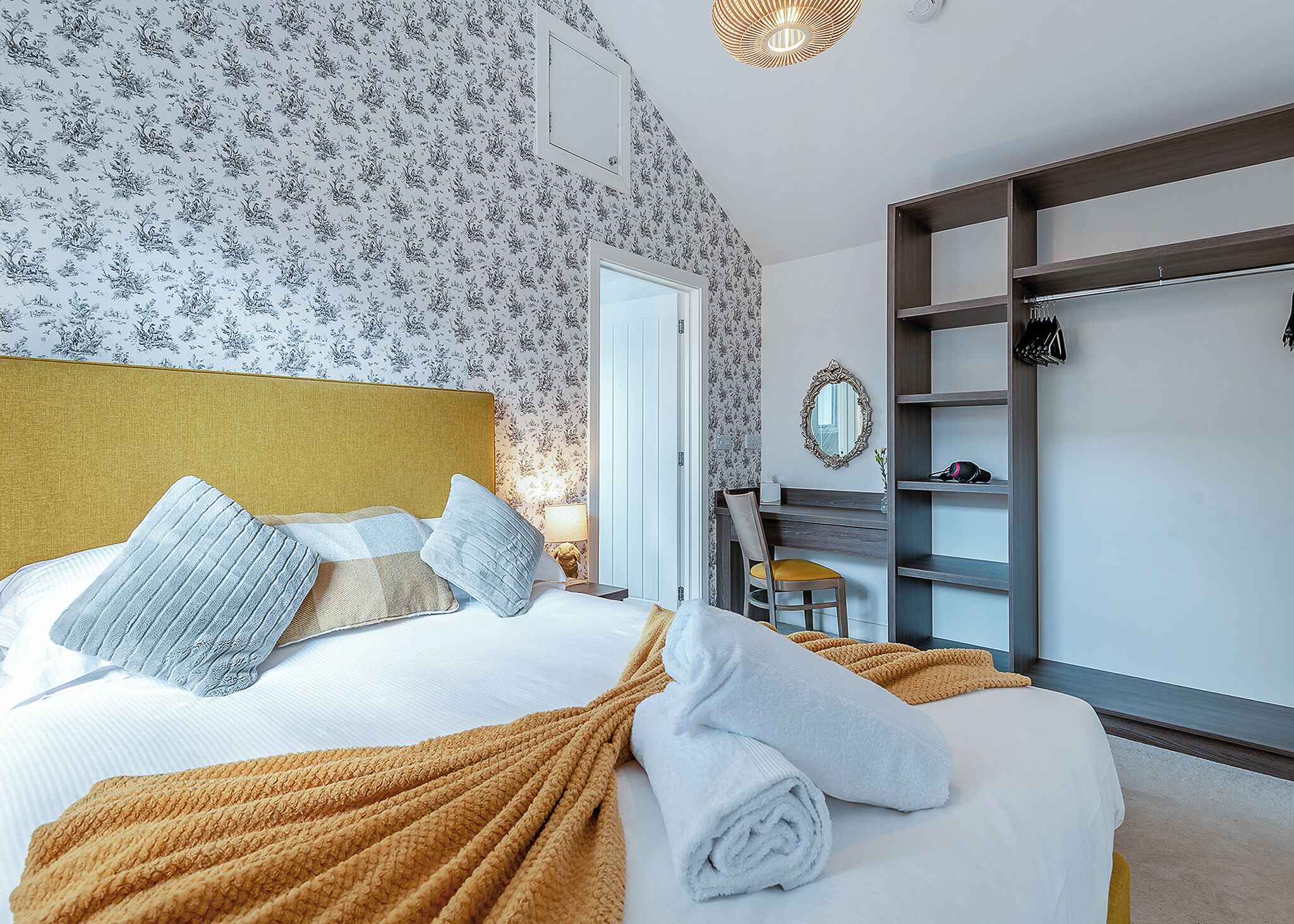 A bedroom with a bed, a desk, a chair, a wardrobe, and a mirror.