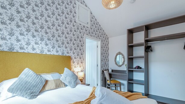 A bedroom with a bed, a desk, a chair, a wardrobe, and a mirror.