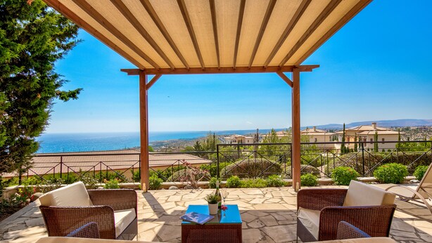 Un espacio de estar al aire libre cubierto con mobiliario de mimbre y vista al mar.