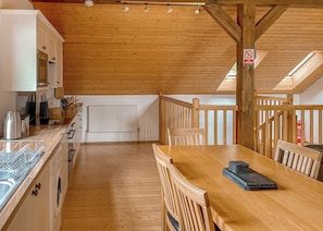 A wooden interior with a dining table, chairs, a kitchen area with cabinets, a radiator, and a wooden railing.