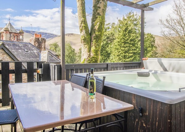 A patio with a hot tub, a table with chairs, and a view of a stone building and trees.