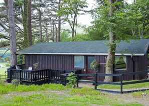 A rustic cabin with a porch, surrounded by trees and a grassy area.