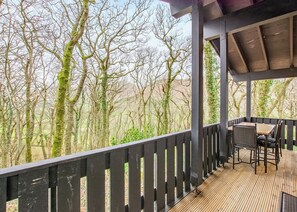 A covered outdoor seating area with a view of trees and a wooden deck. - Very comfortable lodge with one double and one twin. (Millom)