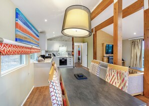 A modern kitchen with white cabinets, a marble backsplash, and a dining area with a wooden table and patterned cushions.