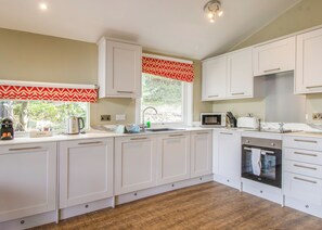 A modern kitchen with white cabinetry, a microwave, a toaster, and a built-in oven. - Very comfortable lodge with one double and one twin. (Millom)