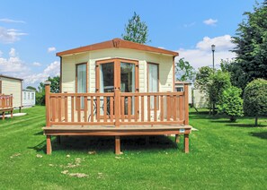 A mobile home with a wooden deck, large windows, and a small porch.