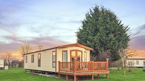 A mobile home with a porch and a large tree nearby. - Holiday home with one double with en suite, and one twin. (Tollerton, York)