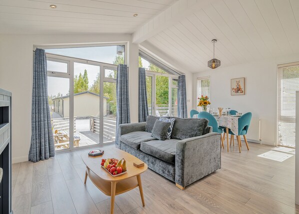 A modern living room with a sofa, dining table, and chairs, large windows, and a view of the outside.