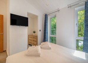 A bedroom with a bed, a TV, a dresser, and a window with curtains.
