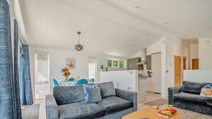 Ein modernes Wohnzimmer mit einem grauen Sofa, einem Holztisch und einer Küche im Hintergrund.