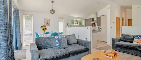 A modern living room with a grey sofa, a wooden coffee table, and a kitchen in the background.