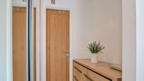 Ein Flur mit einer Holztür, einer weißen Wand und einem Holzschrank mit einer Pflanze darauf.