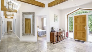 Ein geräumiger Flur mit hoher Decke, Holzbalken, einem großen Spiegel, einem Bett, einer Kommode und einer Tür, die nach draußen führt.