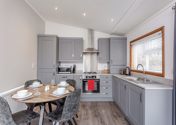 A compact kitchen with grey cabinets, a microwave, a stove, and a sink.