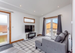 A modern living room with a flat-screen TV, grey sofa, and a large window with curtains.