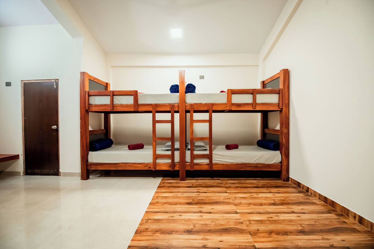Une pièce avec un lit superposé en bois, une porte en bois et un sol carrelé.
