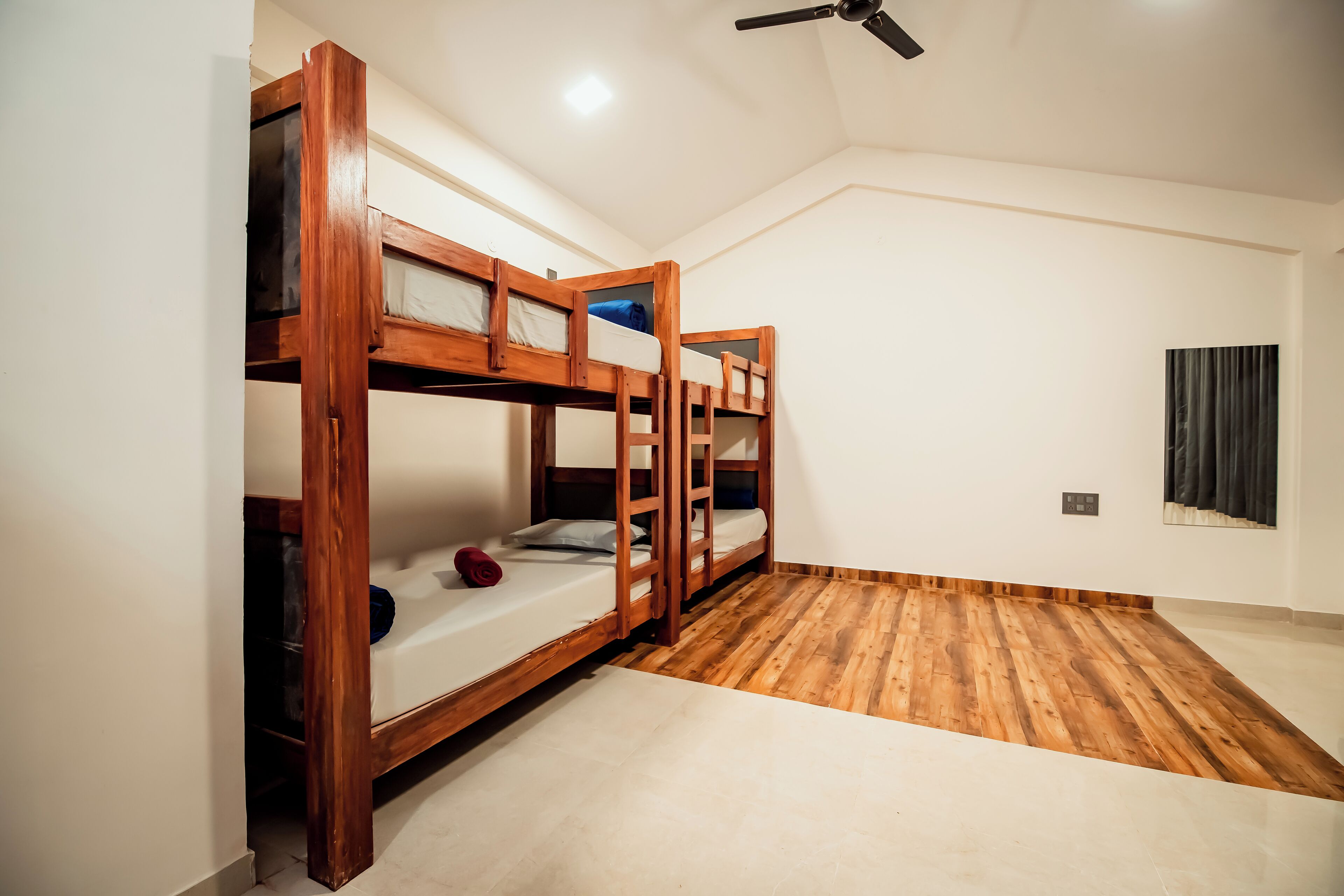 Una habitación con tres literas de madera, un ventilador de techo y una ventana con cortinas.