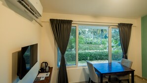Quarto com televisão, mesa com cadeiras, janela com cortinas e ar condicionado.