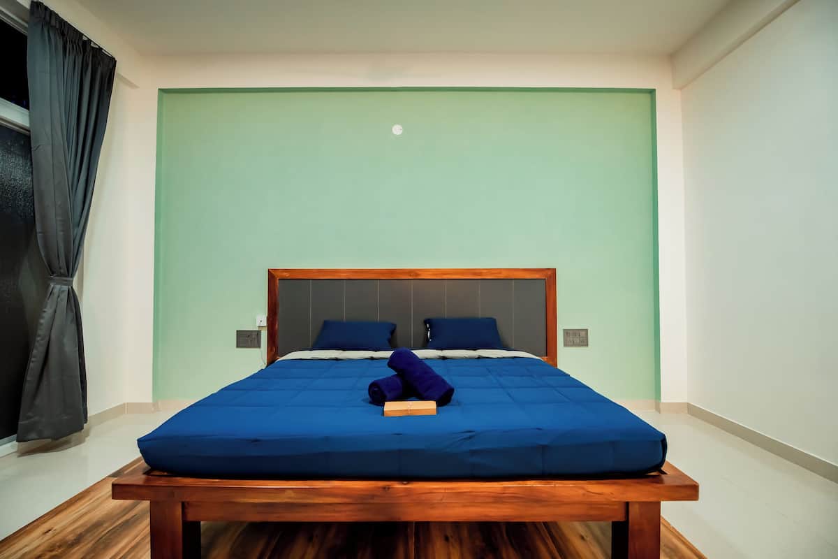 Un lit bien fait, avec une literie bleue et une tête de lit en bois, une table de chevet en bois et un rideau noir à la fenêtre.