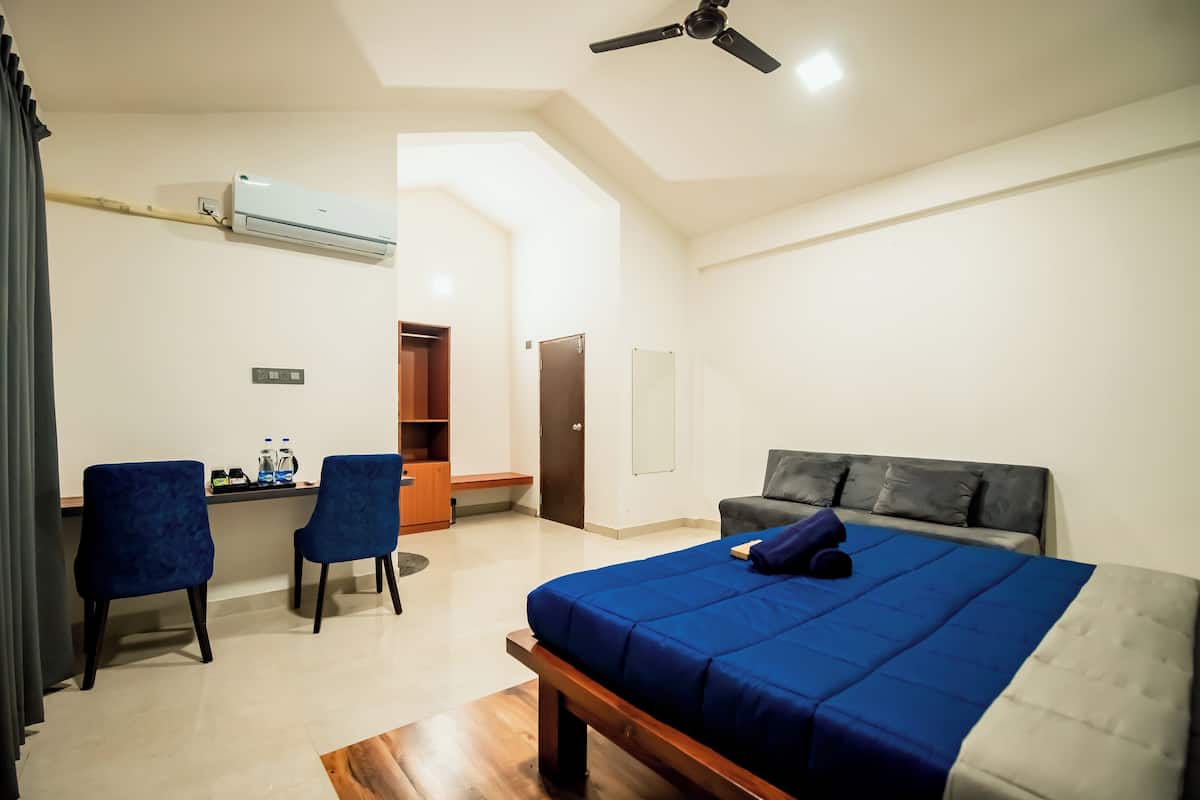Une chambre d’hôtel équipée d’un lit, d’un bureau, de deux chaises, d’un climatiseur, d’un ventilateur de plafond et d’une armoire.