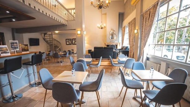 A spacious dining area with multiple tables and chairs, a staircase, and a chandelier. - Galaxy (Kalabaka)