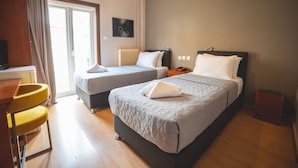 A hotel room with two beds, a desk with a chair, a radiator, and a window with curtains. - Galaxy (Kalabaka)