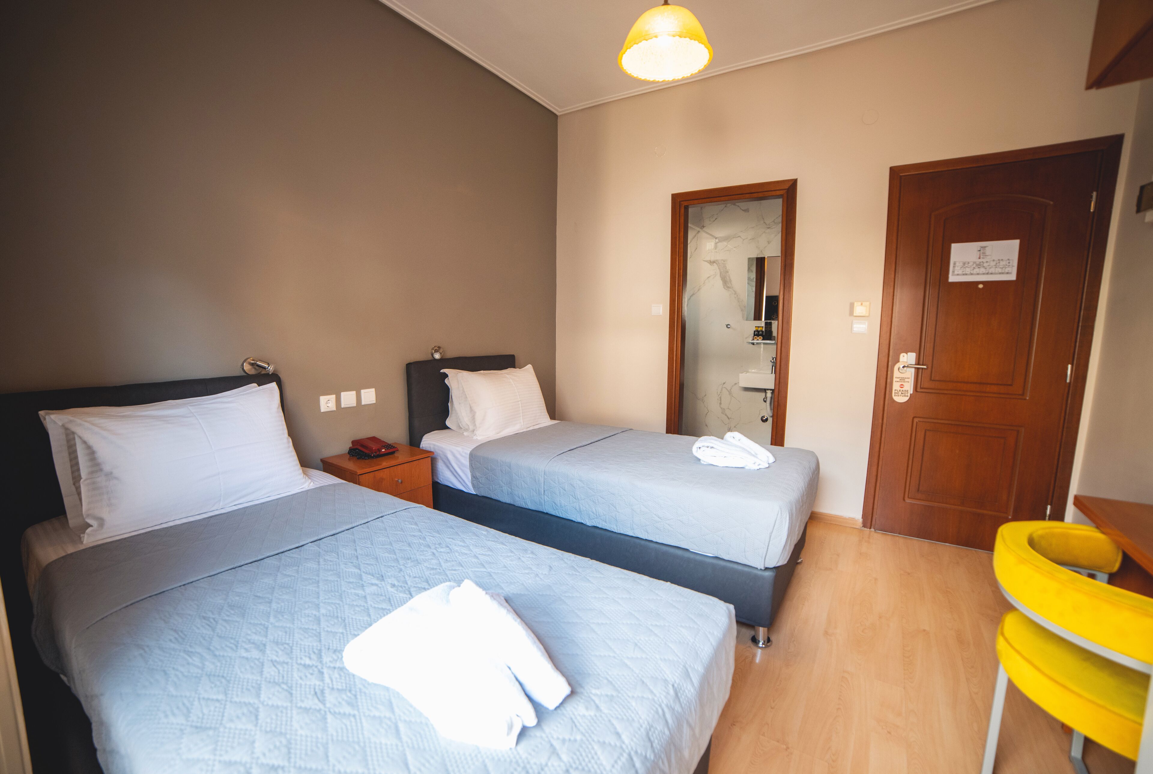 Ett hotellrum med två sängar, en trädörr, en spegel och en gul stol.