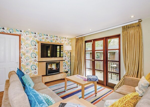 A living room with a sofa, a coffee table, a fireplace, and a large window with curtains. - Traditional lodge with one double and one twin. (Millom)