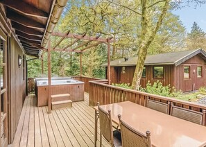 A wooden deck with a hot tub, outdoor seating, and a view of a cabin.