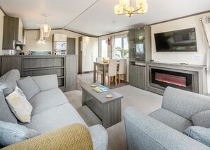 A modern living room with grey sofas, a coffee table, a fireplace, a TV, and a kitchen area with cabinets and a microwave.