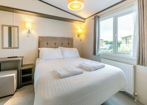 A hotel room with a bed, bedside tables, a mirror, wall sconces, and a window with curtains. - Luxurious 14ft-wide holiday home. (Looe)