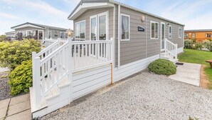 A mobile home with a white deck, a front porch, and a small front yard. - Luxurious 14ft-wide holiday home. (Looe)