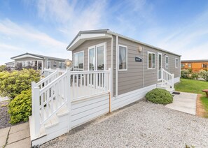 A mobile home with a white deck, a front porch, and a small front yard.