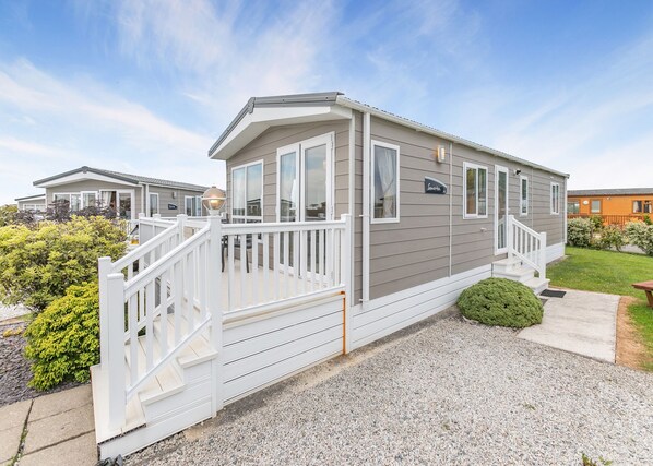 A mobile home with a white deck, a front porch, and a small front yard. - Luxurious 14ft-wide holiday home. (Looe)