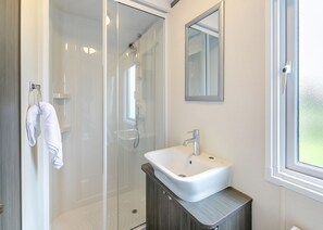 A modern bathroom with a glass shower enclosure, a white sink, and a mirror above it. - Luxurious 14ft-wide holiday home. (Looe)
