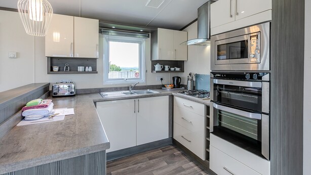 A modern kitchen with a gas stove, built-in oven, microwave, and a large window. - Luxurious 14ft-wide holiday home. (Looe)