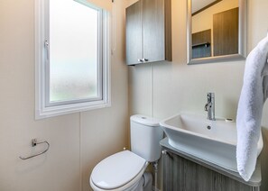 A bathroom with a toilet, sink, and window. - Luxurious 14ft-wide holiday home. (Looe)