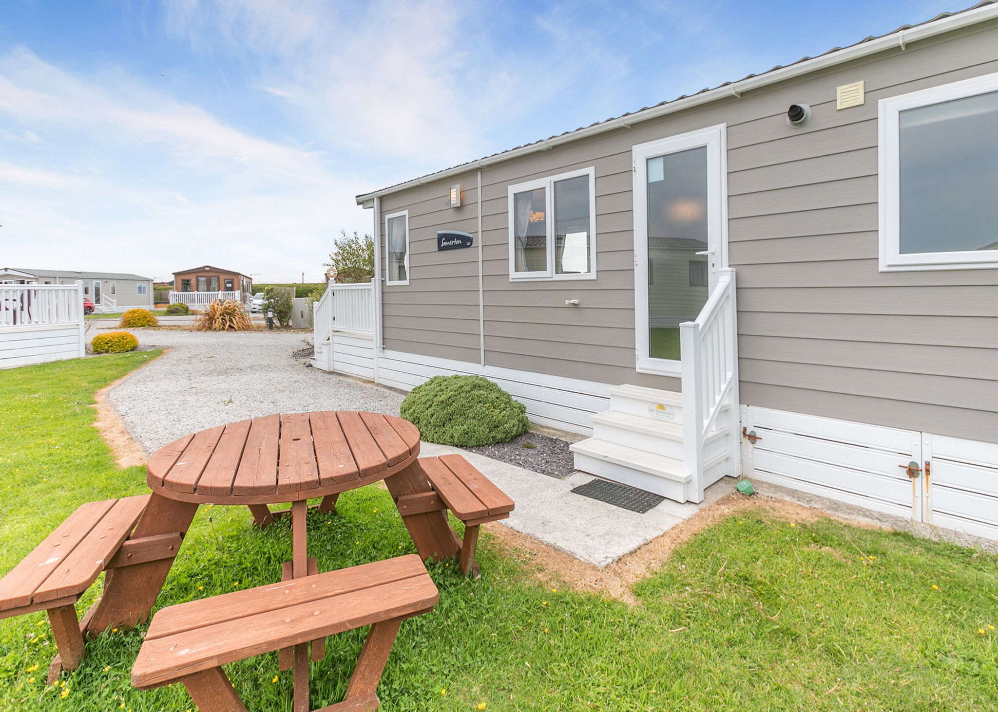 A mobile home with a patio area, a wooden table, and benches.