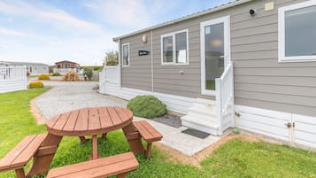 A mobile home with a patio area, a wooden table, and benches.