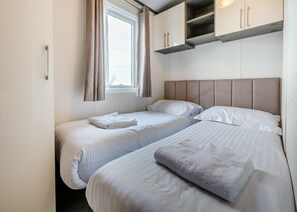 A room with two beds, a window with curtains, and built-in cabinets above the beds.