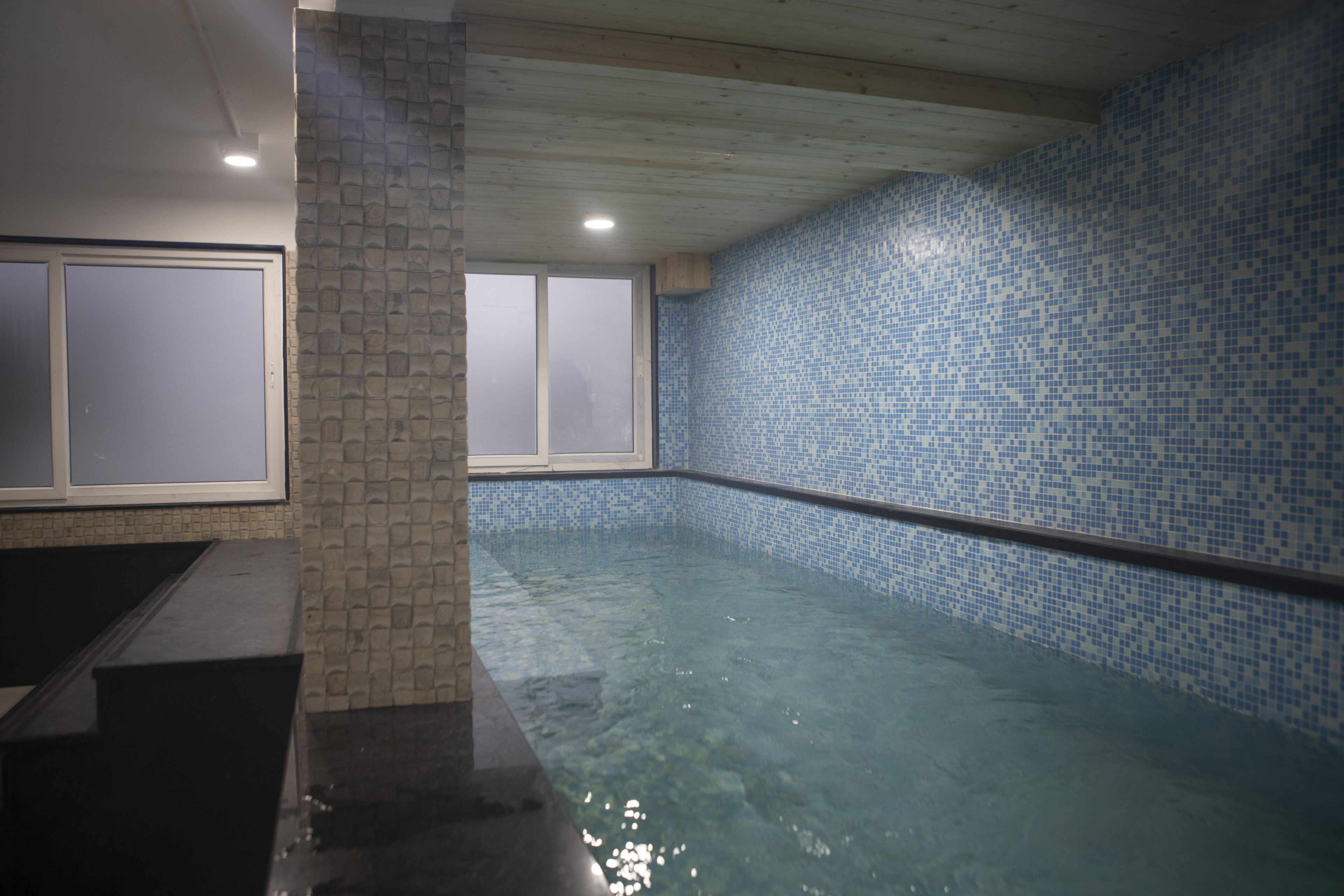 An indoor swimming pool with clear water, tiled walls, and a wooden ceiling.