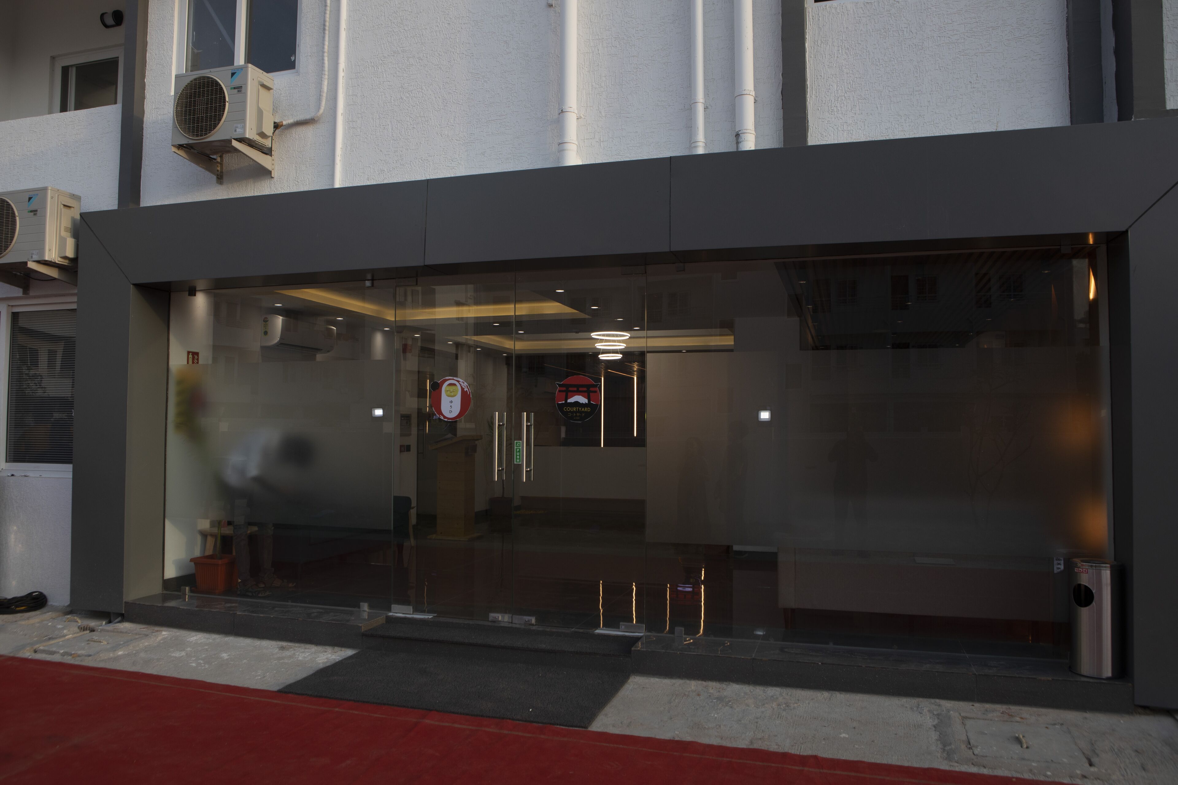 A modern building with a glass entrance, air conditioning units, and a visible fire hydrant.